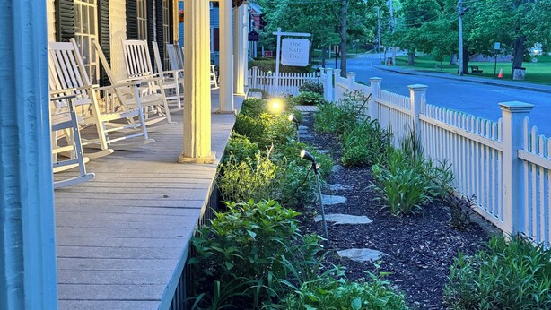 A porch with white rocking chairs, a hanging flower basket, and a sign reading 'One Sixty Five.' - OneSixtyFive (Brunswick)