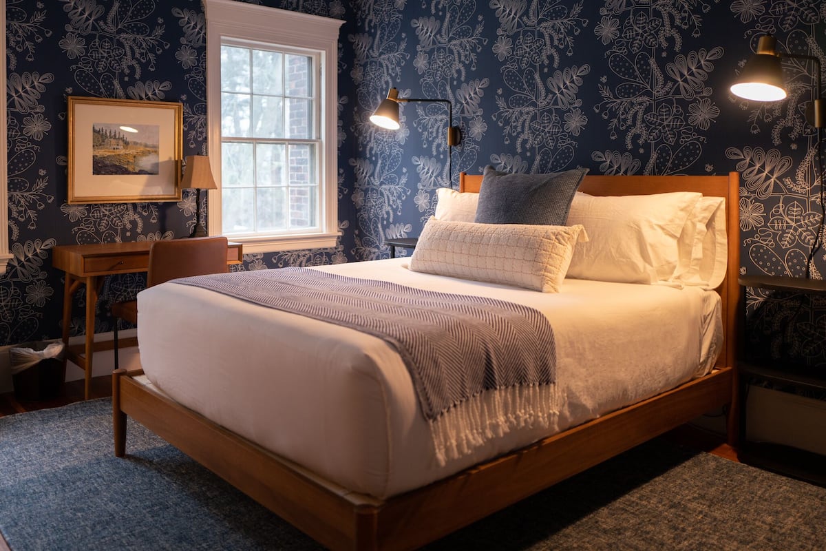 A neatly made bed with a wooden frame, a bedside table with a lamp, and a framed picture on the wall.