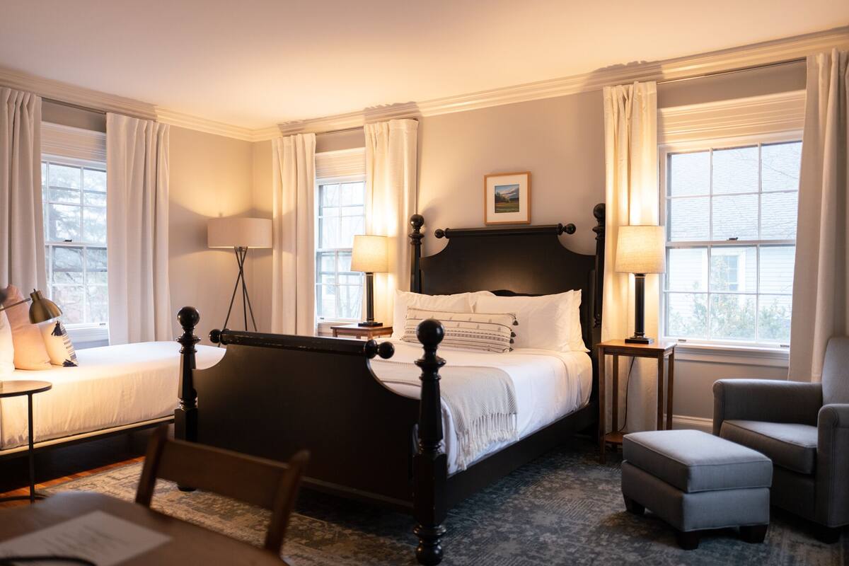 A neatly arranged bedroom with a four-poster bed, bedside lamps, a chair, and a small table.