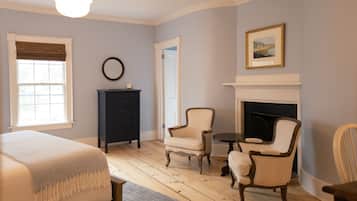 Une pièce comprenant un lit, une cheminée, deux fauteuils, une petite table et une commode.