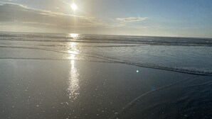 A beach with sunlight reflecting on the wet sand, waves approaching the shore, and a clear sky. - Intimate Heated Pool Side Beach Bungalow! Just steps to the beach! (St. Augustine)