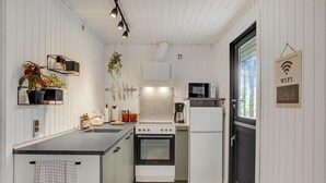 A compact kitchen with white cabinetry, a black refrigerator, a stove, and a microwave. There is a hanging plant, a sink, and a coffee maker. - Awesome home in Ebeltoft with WiFi (Ebeltoft)