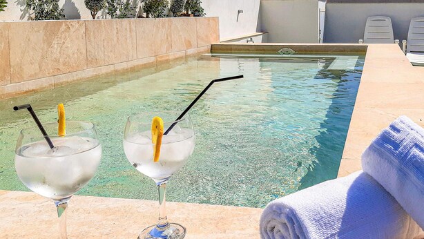 A poolside area with two glasses of a clear beverage, a rolled towel, and a pool.
