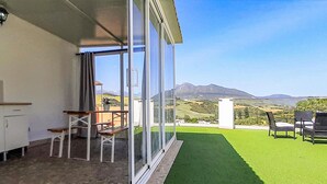A balcony with a view of mountains, a grassy area, and outdoor furniture.