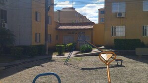 Un terrain de jeux avec des balançoires et une échelle, entouré d’immeubles dotés de balcons et de climatiseurs.