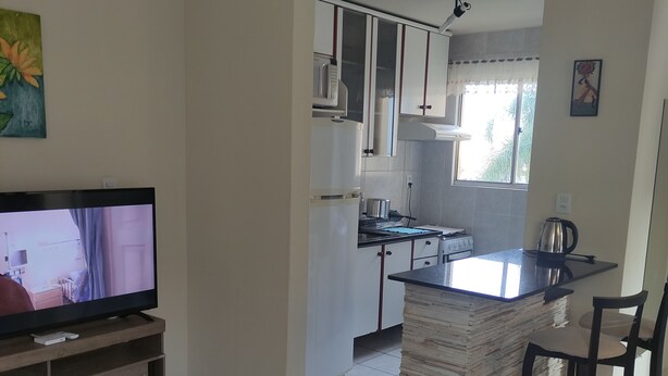 Une cuisine équipée d’un téléviseur, un coin repas avec une table et des chaises, et un ventilateur de plafond.
