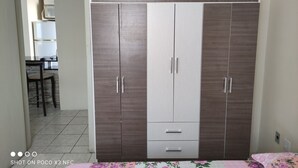 Une chambre dotée d’une grande armoire, d’un lit avec une literie à motifs floraux et d’un espace cuisine visible, équipé d’un four à micro-ondes.