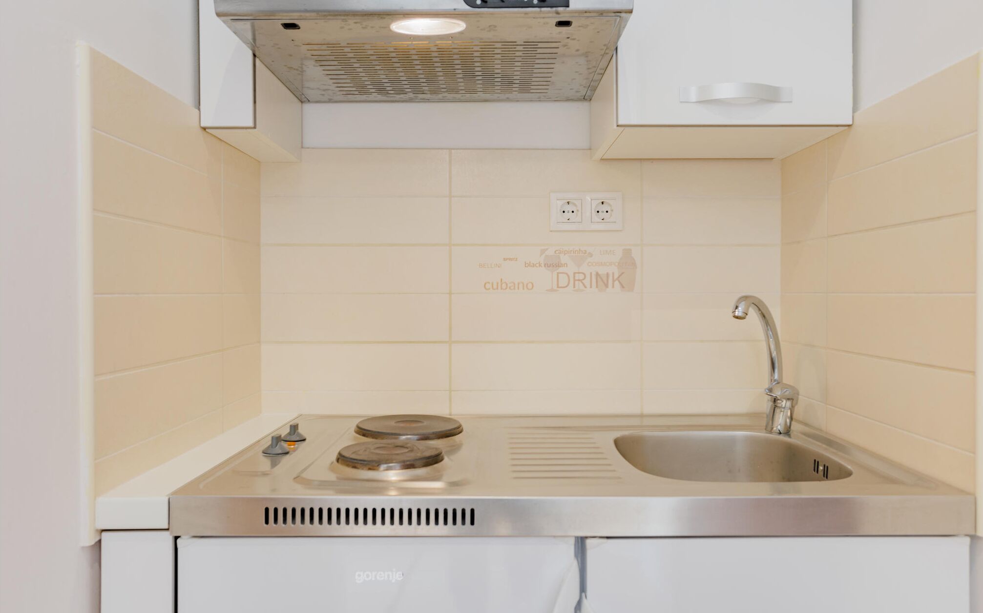 Una cocina con un lavamanos de acero inoxidable, estufa eléctrica doble y campana extractora.