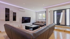 Ein modernes Wohnzimmer mit einem Flachbildfernseher, zwei Sofas, einem Couchtisch und einem großen Fenster.