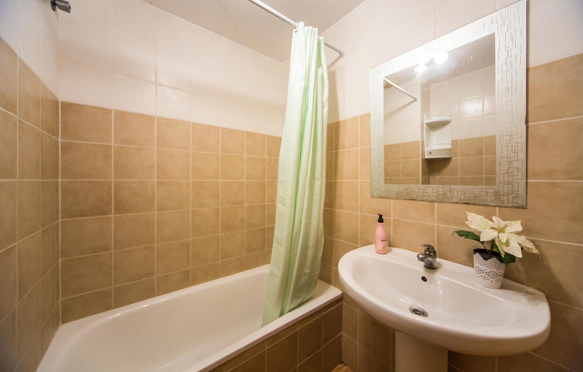 A bathroom with a bathtub, a sink, a mirror, and a shower curtain.