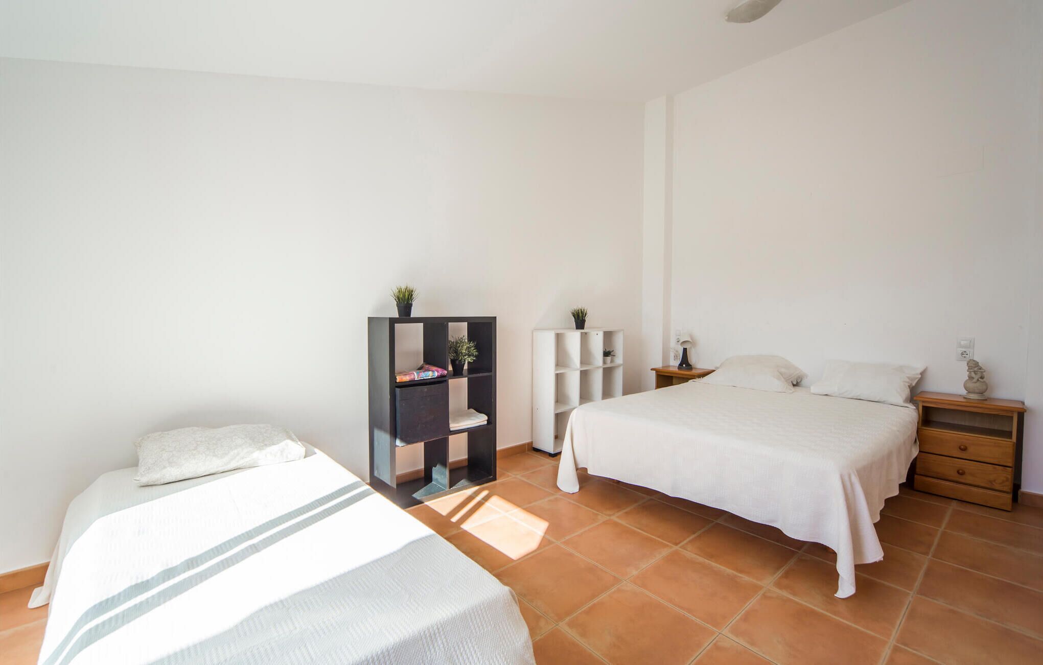 A bedroom with two beds, a nightstand, a bookshelf, and a small table with a lamp.