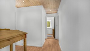 Ein schmaler Korridor mit Holzboden und weißen Wänden, der in einen Raum mit Fenster und Heizkörper führt.