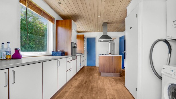 Eine moderne Küche mit Holzboden, einem eingebauten Ofen und einer blauen Tür zu einem weiteren Raum.