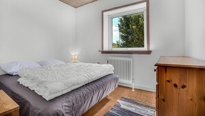 Ein Schlafzimmer mit einem Bett, einer Nachttischlampe, einem Fenster mit Blick auf Bäume, einem Heizkörper und einem Holzschrank.