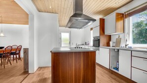 Eine moderne Küche mit einer zentralen Kochinsel, Holzschränken und einem großen Fenster, das für natürliches Licht sorgt.