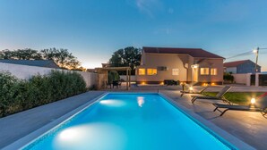 Una piscina con lettini e una casa sullo sfondo.