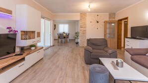 Un soggiorno moderno con un divano, una poltrona e una TV su un mobile basso. Sullo sfondo, un'area pranzo con tavolo e sedie.