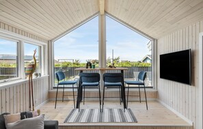 A room with a wooden ceiling, a large window, a TV mounted on the wall, and a table with chairs. - 2 bedroom stunning home in Hjørring (Hjørring)
