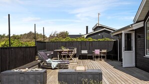 En träaltan med utemöbler, en grillplats och en inhägnad trädgård.