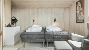 Ett sovrum med två sängar, en stol, ett skrivbord och en inramad tavla på väggen.