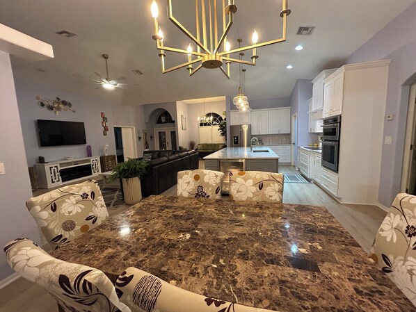 Una cocina moderna con armarios blancos, una isla de granito y un comedor con sillas estampadas de flores.
