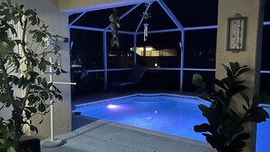 A swimming pool with a geometric structure overhead, surrounded by potted plants, and a framed picture on the wall. - Pool home in a quiet neighborhood (Cape Coral)