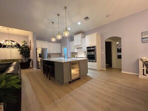 Cocina moderna con una isla central, electrodomésticos de acero inoxidable e iluminación colgante.