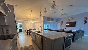 A modern kitchen with a large island, pendant lights, and a dining area with chairs. - Pool home in a quiet neighborhood (Cape Coral)