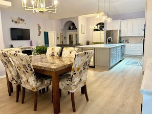 Una cocina moderna con una isla central, un comedor con sillas estampadas y un televisor de pantalla plana montado en la pared.