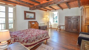 Ein Schlafzimmer mit Holzboden, einem Bett mit gemustertem Überwurf, einem Schminktisch, einem Stuhl, einem kleinen Tisch und einem Kleiderschrank.