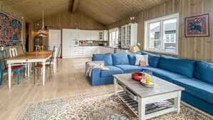 A spacious living room with a blue sofa, wooden dining table, and a kitchen in the background. - 4 bedroom beautiful home in Tisleidalen (Tisleidalen)