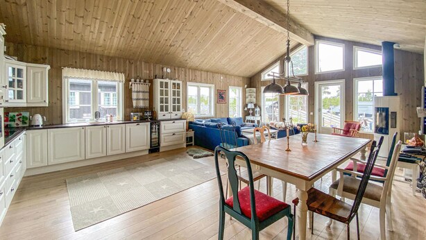 A spacious kitchen with wooden cabinets, a dining area with a wooden table and chairs, and large windows providing natural light. - 4 bedroom beautiful home in Tisleidalen (Tisleidalen)