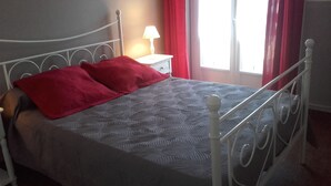 Ein Bett mit Metallgestell, einer roten Decke und einem gemusterten Überwurf.