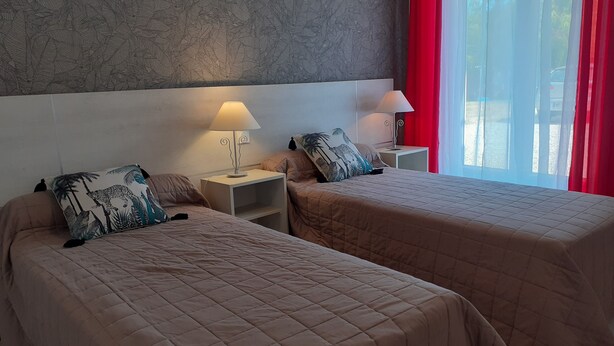 Ein Hotelzimmer mit zwei Betten, jeweils mit gesteppter Bettdecke und passenden Kissen. Nachtische mit Lampen und eine Wand mit Blattmuster sind ebenfalls vorhanden.