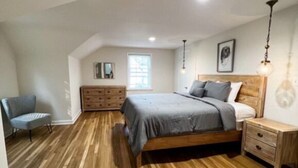 Quarto com piso de madeira, cama, mesa de cabeceira, cômoda e cadeira.
