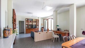 A spacious living area with a wooden entertainment unit, a dining table, and a workspace with a laptop.