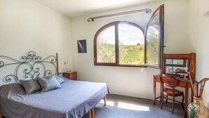 A bedroom with a bed, a desk with a chair, a large window, and a mirror.