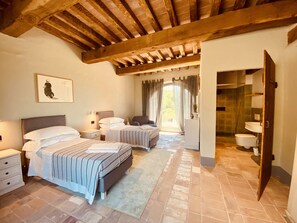 A bedroom with two beds, a nightstand, a dresser, and a bathroom visible through an open door.