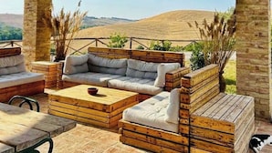 An outdoor patio with wooden furniture, a woven ceiling, and a view of rolling hills. - Beautifully restored Tuscan villa, with private pool and breathtaking views (Monteroni d'Arbia)