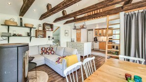Ein gemütliches Wohnzimmer mit einer Couch, einem Esstisch und einer Küchenzeile mit Holzbalken und Schränken.