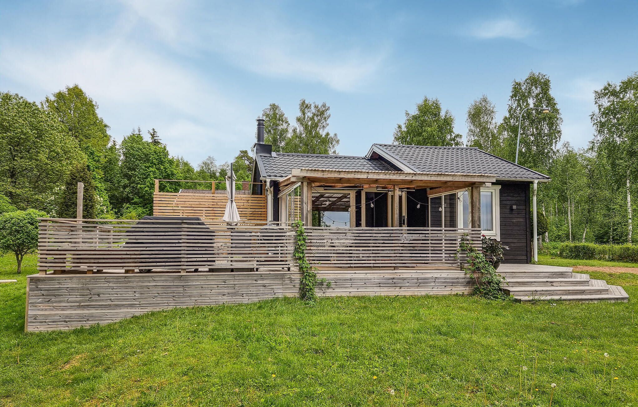 Ett modernt trähus med en inglasad veranda och en skorsten, omgivet av frodig grönska.