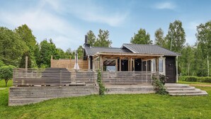 Ein modernes Holzhaus mit überdachter Veranda und Schornstein, umgeben von üppigem Grün.