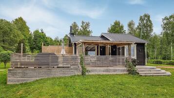 Ett modernt trähus med en inglasad veranda och en skorsten, omgivet av frodig grönska.