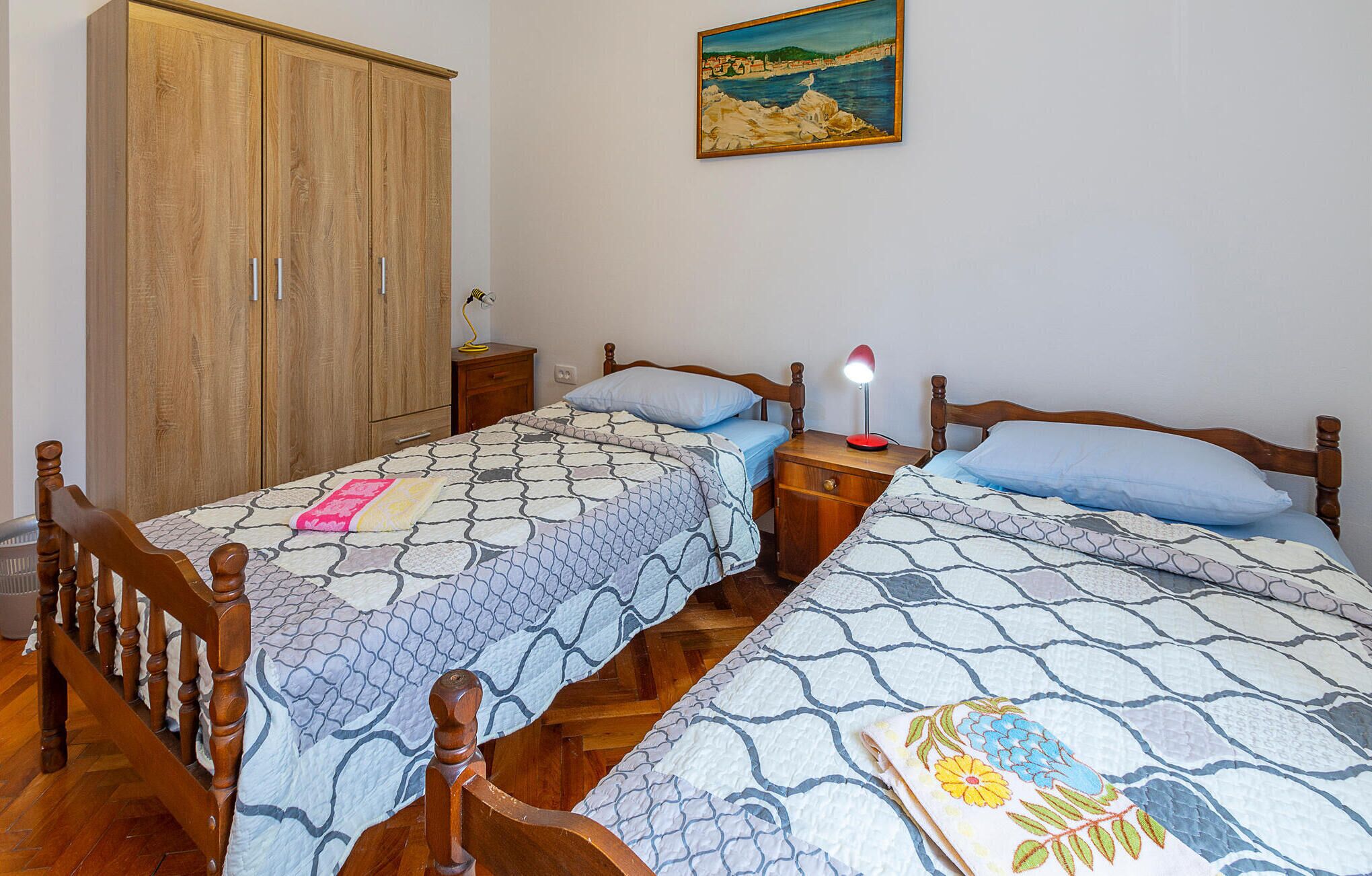 A bedroom with two single beds, wooden wardrobe, and a painting on the wall.