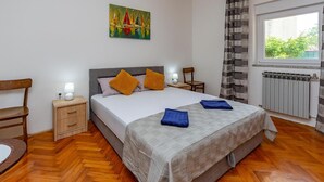 Une chambre bien rangée, avec un lit, des tables de chevet, une chaise, un radiateur et une fenêtre avec des rideaux.