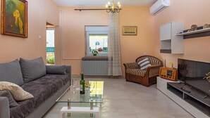 Un salon avec un canapé gris, une table basse en verre, un fauteuil en bois, un meuble pour la télévision et un radiateur.