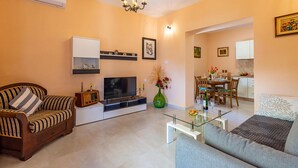 Un salon comprenant un canapé, un téléviseur, une table basse en verre et un coin repas avec une table et des chaises.