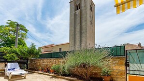 Une haute tour surmontée d’une horloge, un mur de pierre et une clôture verte.