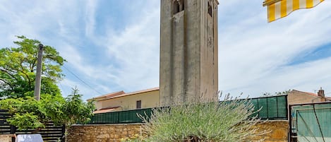 Una torre alta con un reloj, un muro de piedra y una valla verde.