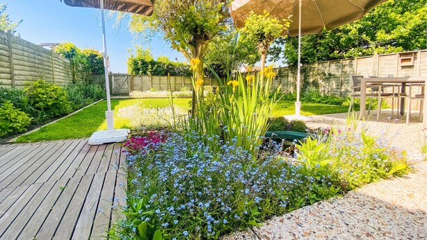 A garden with a wooden deck, a white outdoor heater, and two umbrellas. - 2 bedroom awesome home in Bredene (Bredene)